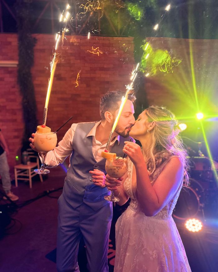 Noivos se beijando e brindando com drinks e velas cintilantes